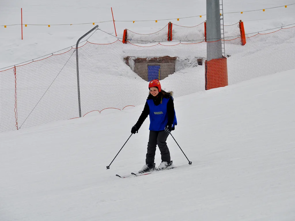 Skifahrer im blauen Leibchen posiert vor einer Liftstütze.